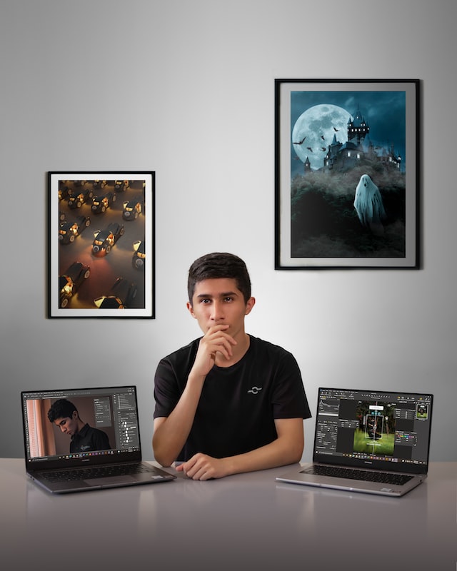man in black t-shirt sitting with two laptops